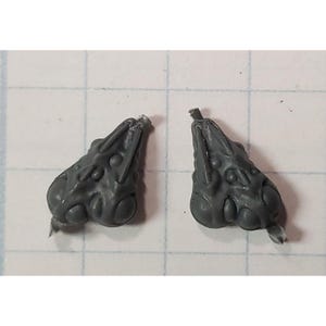 May include: Two gray plastic pieces with a detailed, textured, organic design. The pieces have a pointed end and a rounded, bulbous shape.