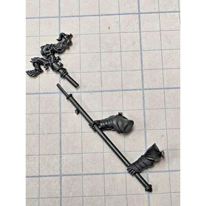 May include: A black plastic miniature hobby component featuring a staff with an ornate, swirling top piece and a long, thin shaft. Two separate hand-like appendages are attached to the shaft, each showing detailed folds and textured surfaces.