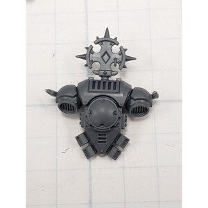 May include: A gray plastic miniature figure torso with a detailed design. The figure has a circular chest piece, shoulder pads, and a decorative headpiece with spikes. The miniature is designed for tabletop gaming.