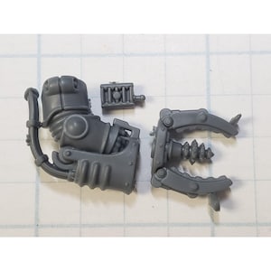 May include: A gray plastic model kit for a robot arm with a drill attachment. The arm has a series of gears and a control panel. The drill attachment has a rotating drill bit.