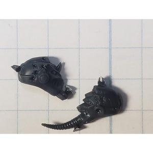 May include: Two gray plastic miniature heads with detailed facial features and intricate designs. One head has a pointed horn on top and the other has a long, thin snout.