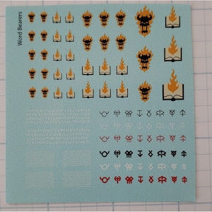 May include: A sheet of waterslide decals for Warhammer 40k featuring Word Bearers icons. The sheet includes multiple images of a demon head with flames, a book with flames, and various symbols. The text "Word Bearers" is printed on the left side of the sheet.