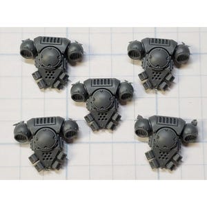 May include: Five gray plastic miniature armor pieces. Each piece features a central circular element, rectangular top, and two rounded side elements. The bottom has a series of small, angled protrusions. The pieces are arranged on a grid.