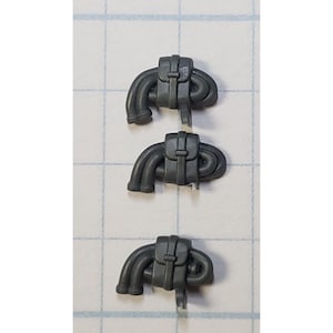 May include: Three gray plastic miniature backpacks with curved tubes attached. Each backpack has a rectangular flap secured by a buckle. The tubes are looped and appear to be part of a larger component.