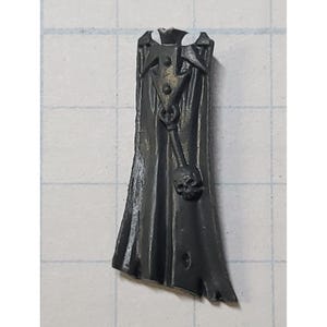 May include: A black plastic miniature cape with a white collar and a skull detail. The cape is designed for use with miniature figures.