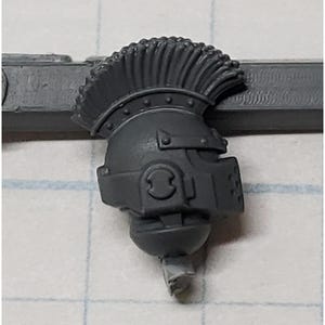 May include: A gray plastic helmet with a mohawk-style crest. The helmet has a visor and a chin strap.