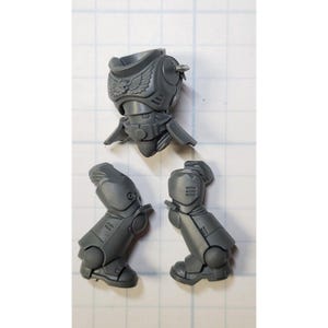 May include: Gray plastic model kit parts for a space marine. The kit includes a torso, two legs, and a helmet. The torso has a sculpted eagle emblem on the chest.