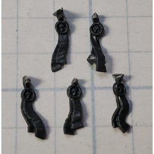 May include: Five small, dark gray plastic components. Each piece has a circular top with a detailed design, a narrow, curved body, and a pointed end. The pieces are scattered on a grid-lined surface.