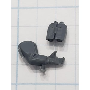 May include: Two gray plastic miniature model pieces. One piece is a bent arm with a hand, and the other is a pair of binoculars. The pieces are on a grid background.