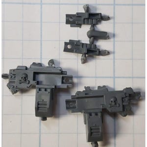May include: Two gray plastic miniature guns with skull and crossbones details. The guns are unassembled and have a sci-fi aesthetic.