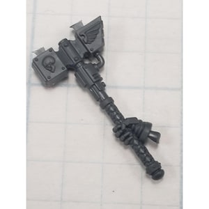 May include: A dark gray miniature war hammer with a skull emblem and winged design. The hammer features a textured handle and detailed mechanical components, likely for a tabletop game or model.