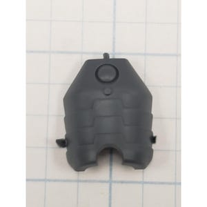 May include: A dark gray plastic component with a geometric design. The piece has a rounded top with a circular indentation and a small protrusion. The bottom features two cut-out sections and two small tabs on the sides. The component is set against a grid background.