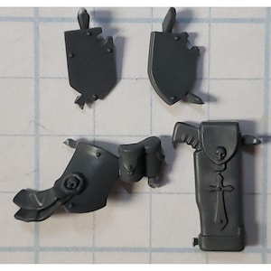 May include: A set of four gray plastic miniatures for a tabletop game. The miniatures include a shield, a sword, a leg piece, and a pouch.