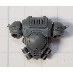 May include: Gray plastic model kit part for a space marine, featuring a backpack with a round vent and a rectangular panel with a series of vents.