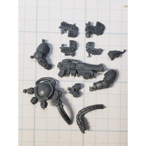 May include: A set of gray plastic miniature figures for a tabletop game. The set includes a weapon, body parts, and a head.