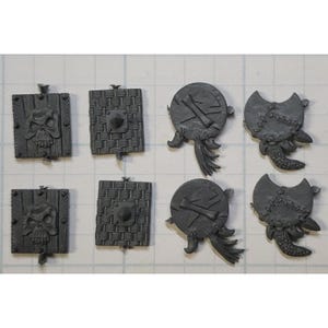 May include: Eight miniature plastic shields with different designs.  Some shields have a skull and crossbones design, others have a woven pattern, and others have a stitched pattern.