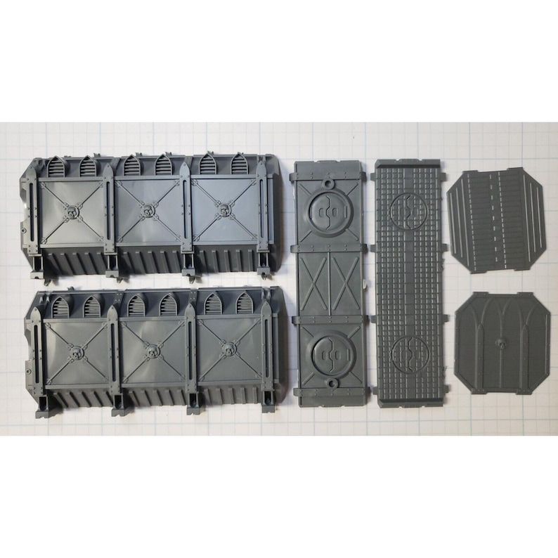 May include: A set of gray plastic model building pieces for a miniature wargame. The pieces include walls, doors, and other architectural details.