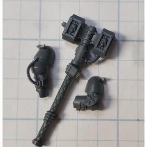 May include: A set of three gray plastic miniature figures for a tabletop game. The figures include a weapon with a skull design, a left arm, and a right arm.