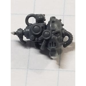 May include: A gray plastic miniature of a mechanical device, possibly a weapon or tool. It features a complex design with circular and angular components, including a nozzle, a mask-like structure, and a curved handle.