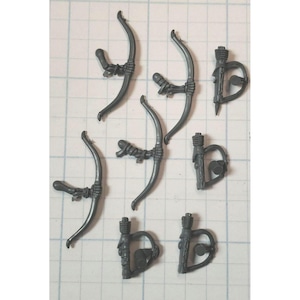 May include: Seven gray plastic miniature bows with arrowheads. The bows are curved and have a string attached. The arrowheads are pointed and have a small detail on the side.