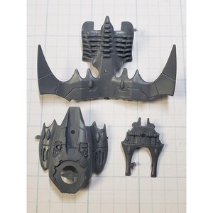 May include: Four gray plastic pieces for a model kit. The pieces are shaped like wings, a torso, and a head. The pieces are detailed with lines and circles.