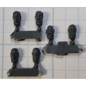 May include: Six gray plastic miniature heads with different facial expressions. The heads are attached to small plastic bases. The bases are arranged in two rows of three. The heads are for use in miniature wargaming.