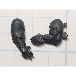 May include: Two gray plastic miniature arms, one with a gloved hand and the other with a sleeve and hand. The arms are detailed with sculpted textures and appear to be part of a larger model kit.