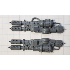 May include: Two gray plastic model weapon parts for a sci-fi miniature game. Each part has a double-barreled gun with a detailed design and a skull symbol.