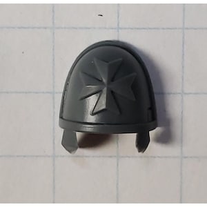 May include: Gray plastic shoulder pad with a raised cross design. The cross is a four-pointed star with a circle in the center.