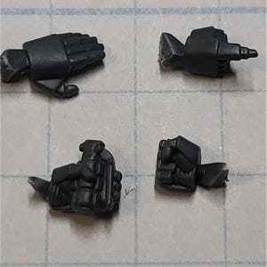 May include: Four black plastic miniature figures with different hand poses. The figures are designed for tabletop gaming or role-playing.