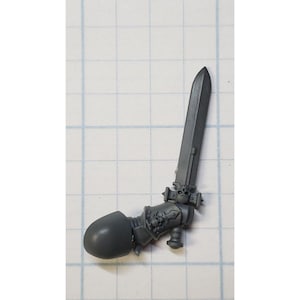 May include: A gray plastic miniature of a sword and hand for a tabletop game. The sword has a skull on the hilt.