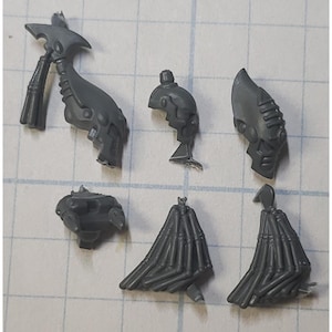 May include: A collection of unpainted, gray plastic miniature parts for a tabletop game. The components include a helmet, torso, weapon, and other detailed pieces, likely for assembling a figure or vehicle.