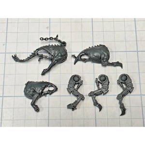 May include: A collection of unpainted dark gray plastic model kit components, including three organic-shaped torso pieces with one featuring a chain attachment, and three mechanical robotic leg assemblies with articulated joints and pointed feet.