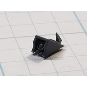 May include: A small, dark gray plastic component with a complex geometric shape. It features a circular opening and several angular protrusions. The piece appears to be a part of a larger assembly, possibly for a model or mechanical device.