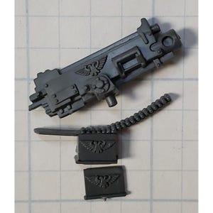 May include: A gray plastic model of a machine gun with a belt of ammunition and two boxes of ammunition. The boxes have an eagle symbol on them.