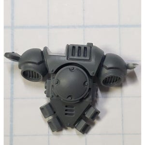 May include: Gray plastic model kit part for a space marine, featuring a detailed back pack with a round engine and vents.