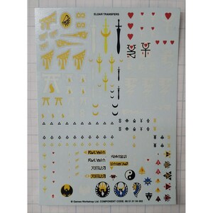 May include: A sheet of white transfer decals for model painting. The decals feature various symbols, including swords, hearts, moons, and a yin-yang symbol. The text "ELDAR TRANSFERS" is printed at the top of the sheet.