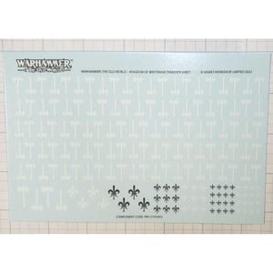 May include: A light blue transfer sheet for Warhammer: The Old World. The sheet features white axe and fleur-de-lis designs. The text "WARHAMMER THE OLD WORLD" is at the top left. The text "WARHAMMER: THE OLD WORLD - KINGDOM OF BRETONNIA TRANSFER SHEET" is at the top.
