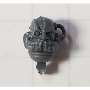 May include: A gray plastic miniature head with a detailed helmet and a single eye. The helmet has a small antenna and a pipe coming out of the side. The head is designed for use in a tabletop wargame.