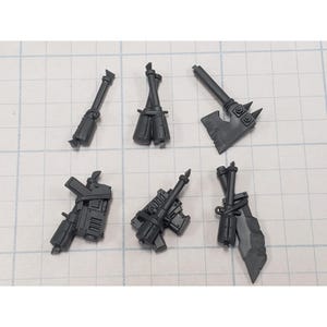 May include: A collection of six unpainted dark gray plastic miniature weapon components. The set includes a long staff, a pair of cylindrical canisters, a bladed axe, two distinct handheld firearm models, and a large serrated blade with a handle.