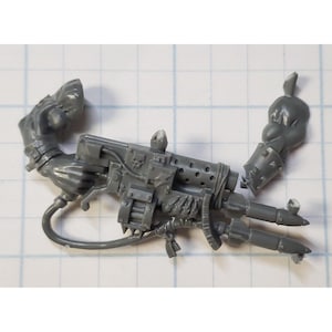 May include: A gray plastic model kit of a futuristic weapon with a barrel, a handle, and a scope. The weapon has a variety of details, including a belt, a handle, and a scope.