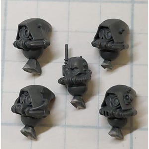 May include: Five unpainted gray plastic miniature heads. Four heads feature hooded helmets with integrated breathing apparatuses. The central head is a bare helmet with a small antenna and a breathing mask. These are small gaming components.