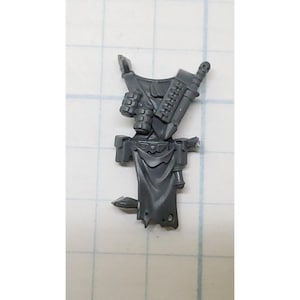 May include: Gray plastic miniature of a space marine torso with a backpack, pouches, and a knife. The miniature is designed for tabletop wargaming.