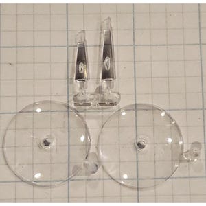 May include: Two clear plastic model ship parts, each with a small, raised, silver design. Two clear plastic round bases with a small hole in the center.