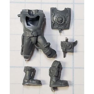 May include: Gray plastic miniature parts for a model kit. The parts include a torso, legs, boots, a shield, and a weapon.