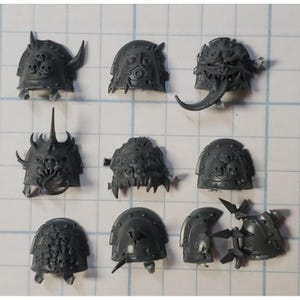 May include: Ten plastic miniature shoulder pads for a tabletop wargame. The shoulder pads are gray and feature various skull and demon designs.