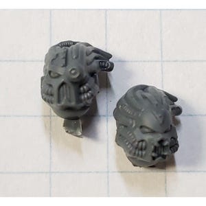 May include: Two gray plastic miniature heads with detailed sculpting, resembling futuristic helmets with intricate designs.