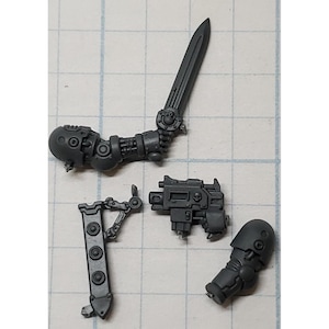 May include: A collection of unpainted, gray plastic miniature parts, including a sword, arm, gun, and leg. The sword has a detailed hilt and blade. The arm is mechanical. The gun has a detailed design. The leg is segmented.