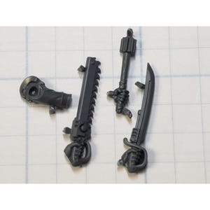 May include: A collection of dark gray miniature weapons, including a chainsaw, a sword, and a mace. The weapons are designed with intricate details and are likely for a tabletop game or model kit.