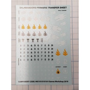 May include: A sheet of Salamanders Primaris transfer decals. The sheet includes vehicle transfers, squad numbers, chapter badges, and other symbols in silver, gold, and black. Text includes "Salamanders Primaris Transfer Sheet" and "Games Workshop 2019".